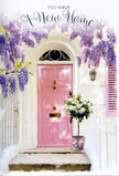 This image portrays a beautifully styled Islington doorway where flowers transform a simple entrance into a heartfelt welcome. A pastel pink front door, painted in a calm, soothing blush, forms the focal point of the scene. Light falls gently across it, suggesting a serene day in one of Islington's quieter streets just off Upper Street or close to Highbury Fields. Around the door, abundant wisteria drapes in languid, lavender cascades. Each trailing stem carries clusters of tiny blossoms that fade from deeper purple tones at the centre to softer lilac at the edges, creating a natural, romantic curtain. The surrounding whitewashed walls are lightly textured, reflecting the light in soft, uneven patches and holding the shadows of the wisteria in delicate patterns. A painted shutter to one side echoes the door's pastel mood, reinforcing the harmony of the façade. Resting neatly on the doorstep is a grey tin bucket with a subtle, brushed finish. Tied around its base is a pink satin ribbon, forming a gentle bow whose trailing ends lie softly against the metal. Bursting from the bucket is a generous bouquet of creamy white roses, their flowers full and open, each petal curving outward in thick, velvety layers. Threads of fresh green foliage weave between the roses, giving the arrangement structure, depth, and a hint of garden freshness. The overall composition looks like a thoughtful housewarming gift from a local Islington florist, perfect for celebrating a move into a new flat near Angel or Essex Road. It conveys an atmosphere of welcome, optimism, and the simple but powerful comfort that carefully arranged flowers can bring to a new home.